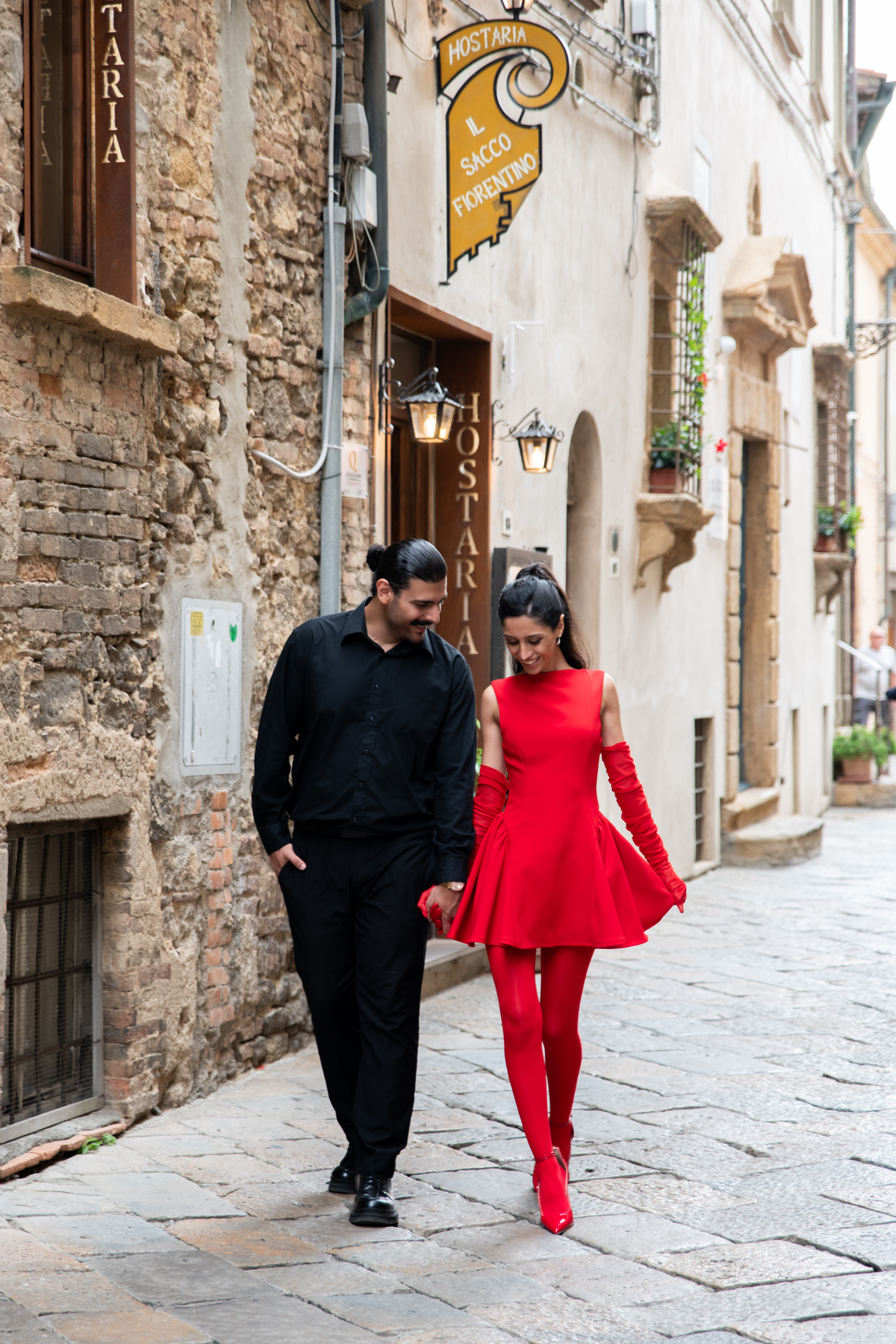 A stylish couple walking hand-in-hand down a historic cobblestone street.