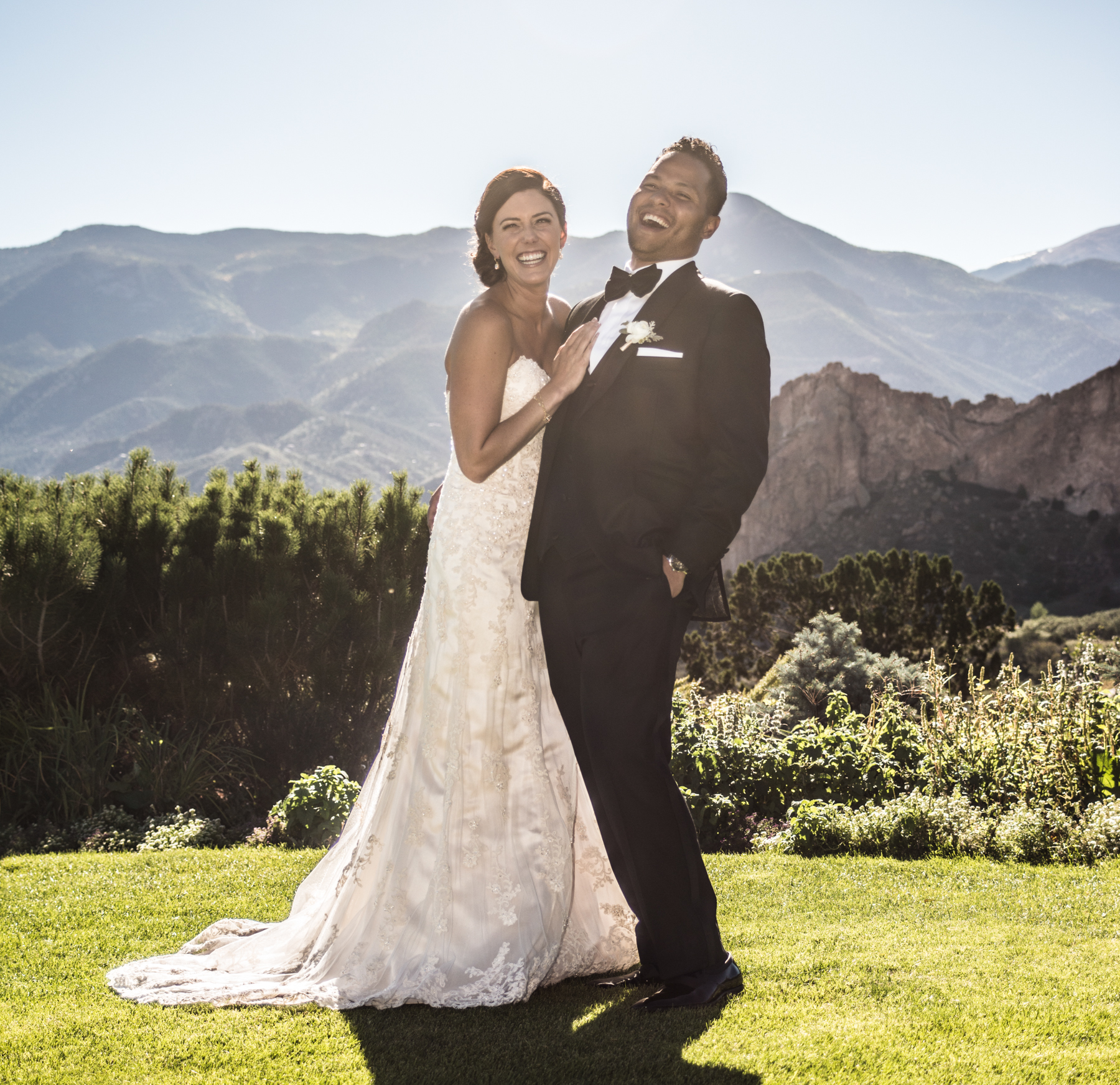 Bride and groom laughing together outdoors with mountain backdrop.
