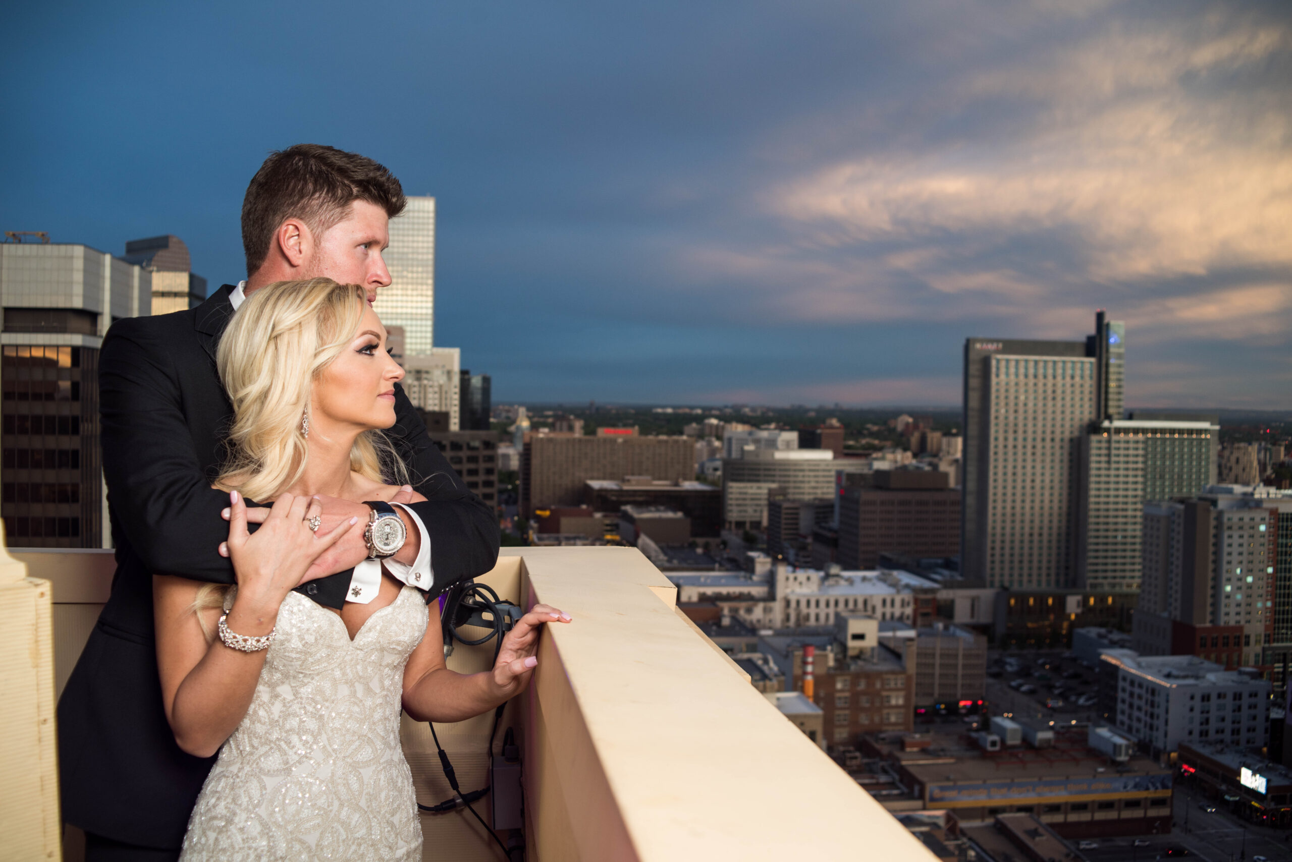 Bride and groom embracing on a city rooftop at dusk overlooking the skyline.
